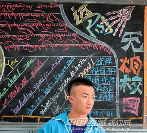 这是高二学生罗布在藏汉英三种文字书写的黑板报前.